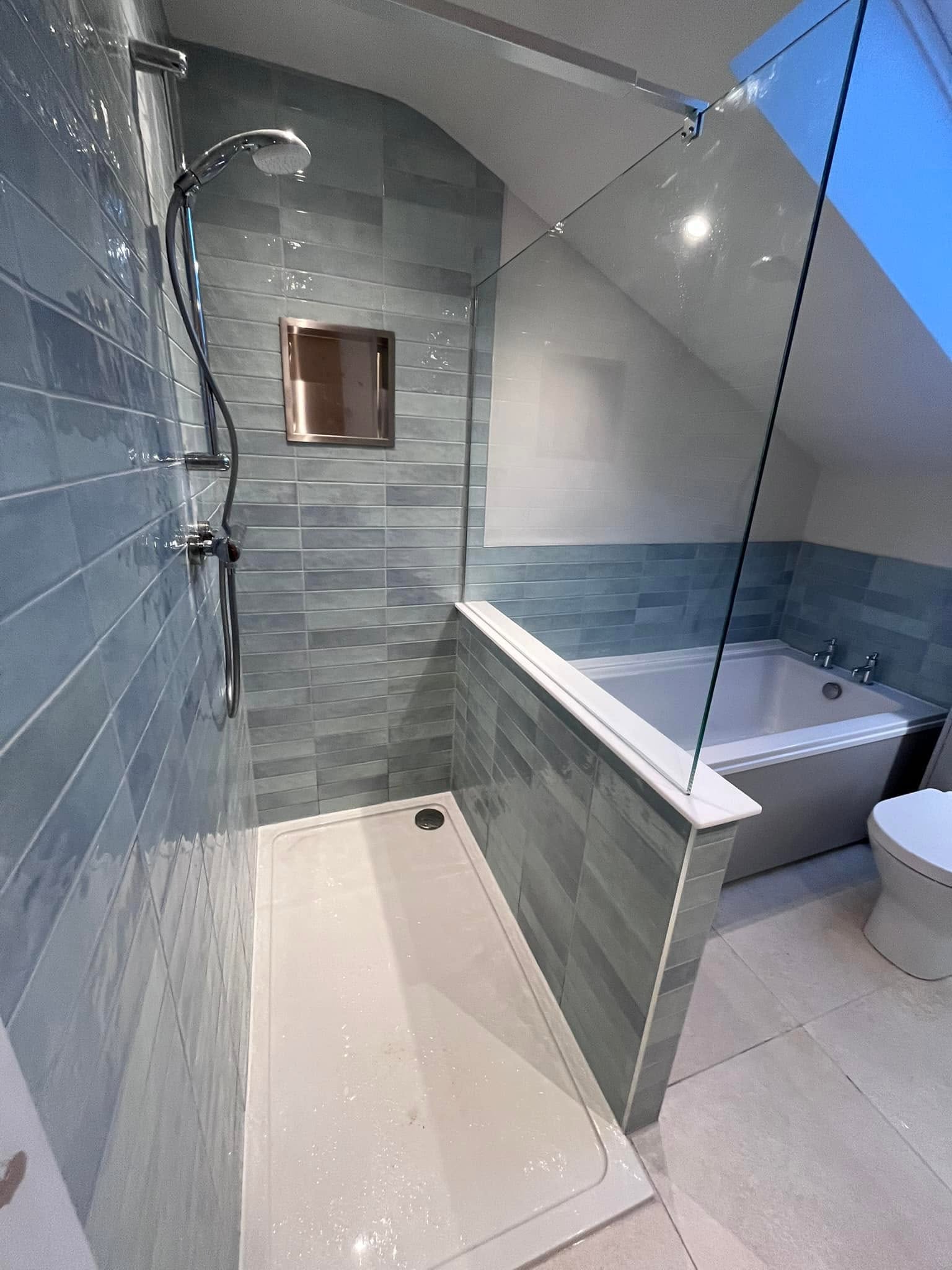 Loft bathroom shower with blue metro tiles, recessed niche and a bath beyond